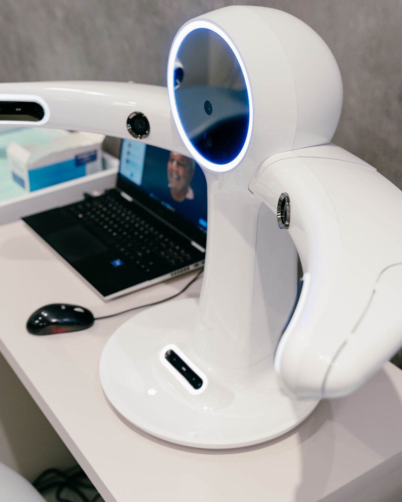 3D diagnostic imaging scanner on a clinic desk, connected to a laptop showing a patient scan