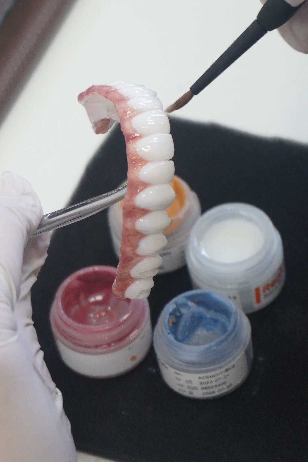 Dental laboratory technician hand-finishing a prosthetic tooth arch with shading pigments