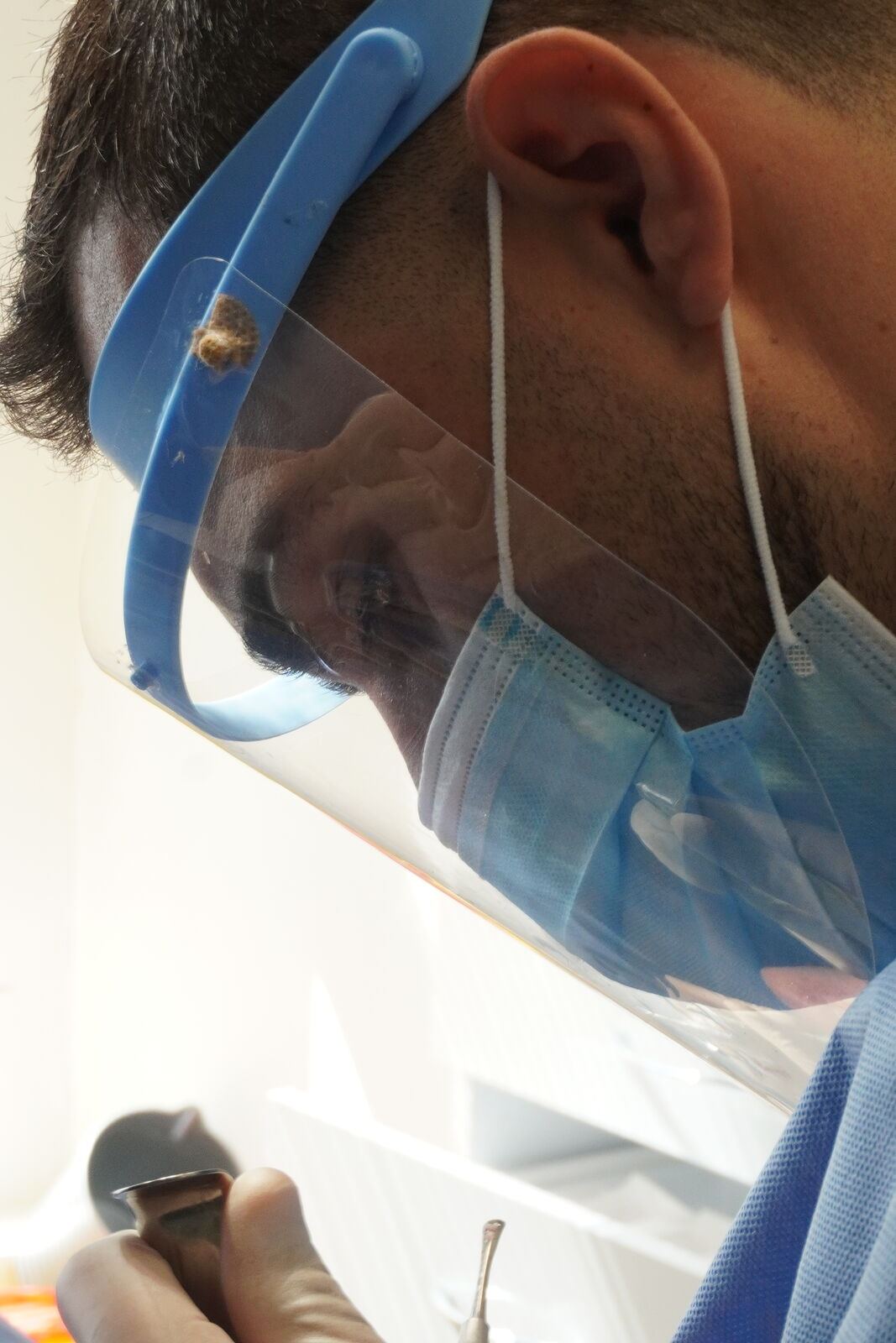 Close profile of a clinician wearing a face shield and mask, holding a dental instrument